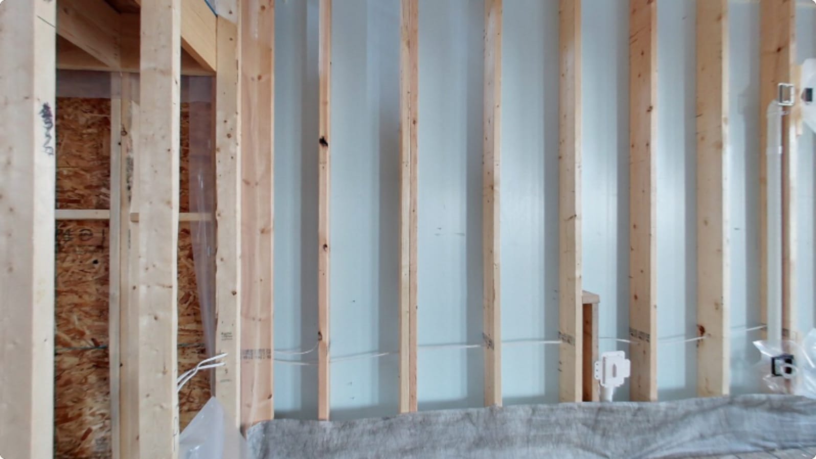 Living-room wall in bare studs with wiring run — opening view of the pre-drywall stage