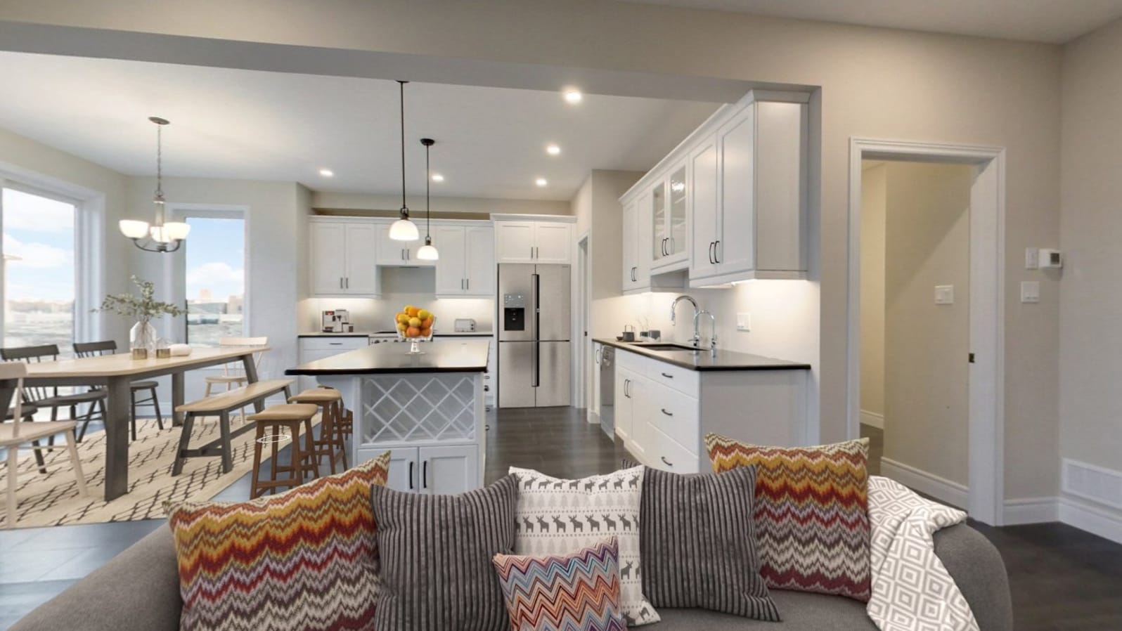 The same space furnished and staged — sofa piled with pillows, dining set on a rug, and styled kitchen island in the opening view of the staged stage